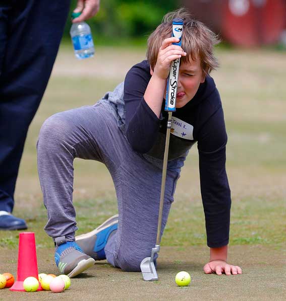 Young boy on a knee sticky out his tongue while lining up a putt.